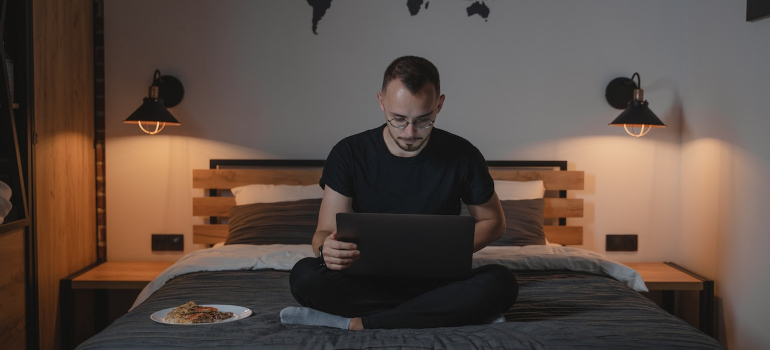 Čovek na krevetu koji drži laptop u krilima